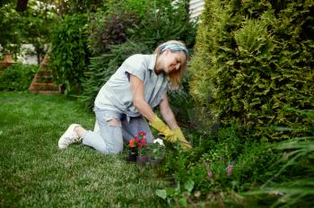 Woman with hoe grows flowers in the garden. Female gardener takes care of plants outdoor, gardening hobby, florist lifestyle and leisure