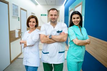 Three smiling doctors in uniform standing in clinic corridor. Professional medical specialist in hospital, laryngologist or otolaryngologist, gynecologist or mammologist, surgeon