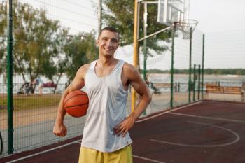 Muscular basketball player on outdoor court. Male athlete in sportswear holds ball on streetball training