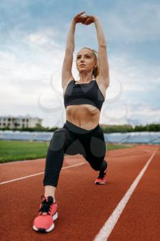 Female jogger in sportswear, training on stadium. Woman doing stretching exercise before running on outdoor arena