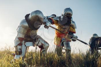 Medieval knights in armor and helmets fight with sword and axe. Armored ancient warrior in armour posing in the field