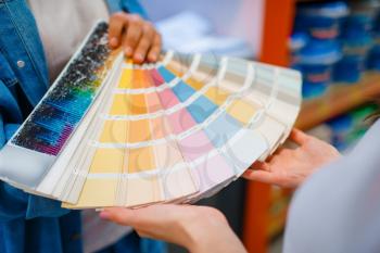 Young couple holds color palette in hardware store. Male and female customers look at the goods in diy shop