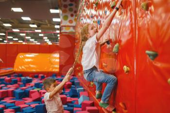 Children quarrels on climbing wall in the entertainment center. Girls and boy leisures on holidays, childhood happiness, happy kids on playground