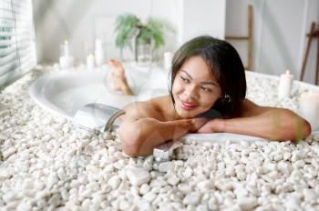 Beautiful woman, relaxation in bath with milk. Female person in bathtub, beauty and health care in spa, wellness treathment in bathroom, pebbles and candles on background