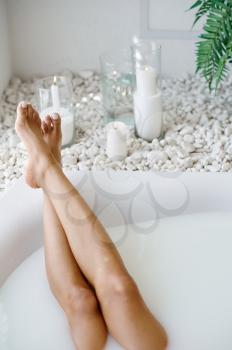 Young woman relax, skincare in bath with milk. Female person in bathtub, beauty and health care in spa, wellness treathment in bathroom, pebbles and candles on background