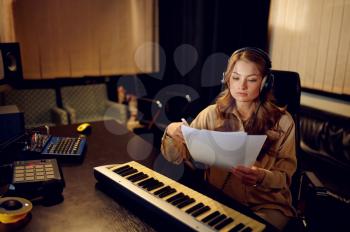 Female sound engineer in headphones, recording studio interior on background. Synthesizer and audio mixer, musician workplace, creative process