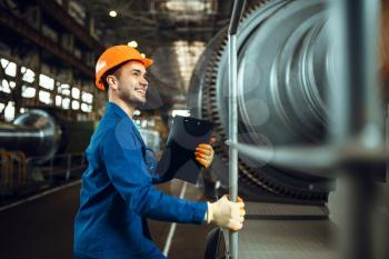 Male worker with notebook, large turbine on background, plant. Industrial production, metalwork engineering, machines manufacturing