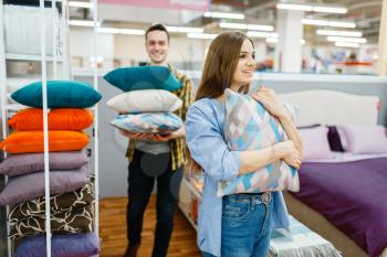 Young love couple holds pillows in furniture store. Man and woman looking samples for bedroom in shop, husband and wife buys goods for modern home interior