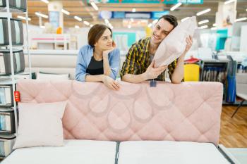 Young love couple poses at the pink couch in furniture store. Man and woman looking samples for bedroom in shop, husband and wife buys goods for modern home interior