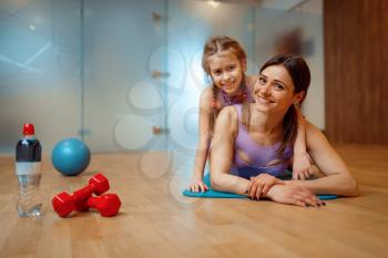 Mother and daughter lying on mat together in gym, fitness workout, gymnastic. Mom and little girl in sportswear, joint training in sport club