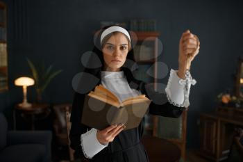 Young nun in a cassock with a cross around her neck holds a book. The sister is preparing for pray in the monastery
