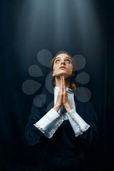 Young nun in a cassock prays on light over her head. The sister in the monastery, religion and faith, religious people