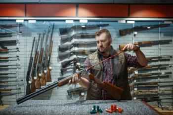 Man cleans rifle barrel at counter in gun shop. Euqipment for hunters on stand in weapon store, hunting and sport shooting hobby