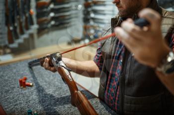 Man cleans rifle barrel at counter in gun shop. Euqipment for hunters on stand in weapon store, hunting and sport shooting hobby