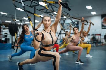 Group of muscular women doing exercise in gym. People on fitness workout in sport club, athletic girls in sportswear on training indoors