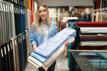Woman holds fabric in textile store. Shelf with cloth for sewing on background, clothing patterns choice in shop, seamstress