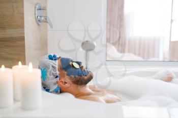 Man applies face mask and relax in bath with foam, morning hygiene. Male person resting in bathroom, skin and body treatments procedures