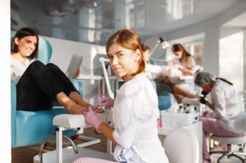Two girlfriends, pedicure process in beauty salon. Professional beauticians and female customers, toenail care in spa studio