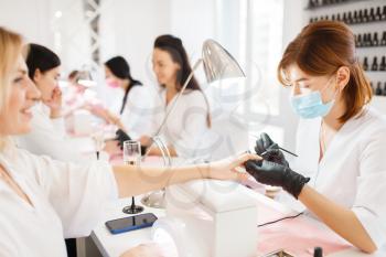 Group of women relax on manicure procedure in beauty salon. Professional beautician and female customers, nail care in spa studio, fingernail treatment