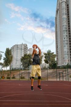 Basketball player makes a throw on outdoor court. Male athlete in sportswear shoots on streetball training, jump in action