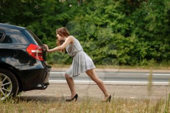 Woman pushing broken car on road, breakdown. Crashed automobile or emergency accident with vehicle, trouble with engine on highway