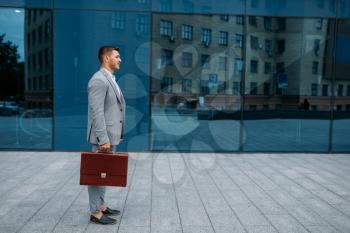 Successful businessman with briefcase at the office building in downtown. Lucky business person in suit, urban style