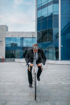 One businessman in funny glasses poses on bicycle at the office building in downtown. Business person riding on eco transport on city street