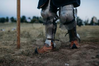 Medieval knight legs in metal armor, back view, great tournament. Armored ancient warrior in armour posing in the field