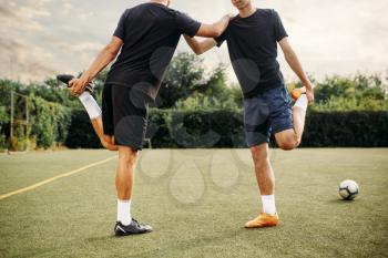 Two soccer players doing stretching exercise on the field. Football training on outdoor stadium, team workout before game