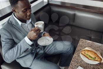 Young negro businessman having lunch in office cafe. Successful business person drinks coffee in food-court, black man in formal wear