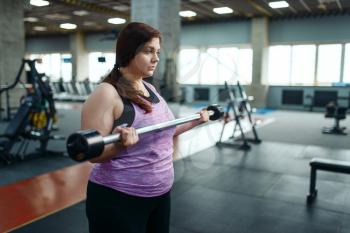 Overweight woman poses with dumbbells on brench in gym, active training. Obese female person struggles with excess weight, aerobic workout against obesity, sport club