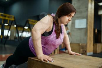 Overweight woman doing push ups exercise in gym, active training. Obese female person struggles with excess weight, aerobic workout against obesity, sport club