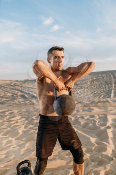 Male athlete sitting on sand after workout in desert at sunny day. Strong motivation in sport, strength outdoor training