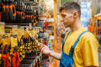 Male builder choosing pliers at the shelf in hardware store. Constructor in uniform look at the goods in diy shop