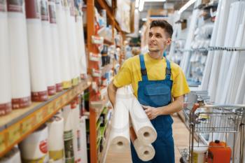 Male builder with roll of wallpapers in hardware store. Constructor in uniform look at the goods in diy shop