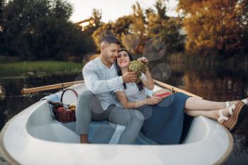 Love couple hugs in a boat on quiet lake at summer day. Romantic meeting, boating trip, man and woman walking along the river