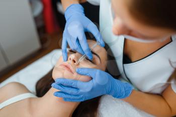 Cosmetician in gloves gives face botox injections to female patient on treatment table. Rejuvenation procedure in beautician salon. Doctor and woman, cosmetic surgery against wrinkles