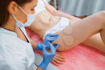 Cosmetician in gloves gives botox injection in the thigh to female patient on treatment table. Rejuvenation procedure in beautician salon. Doctor and woman, cosmetic surgery