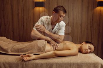 Male masseur rubbing hands to slim woman in towel, professional massage. Massaging and relaxation, body and skin care. Attractive lady in spa salon