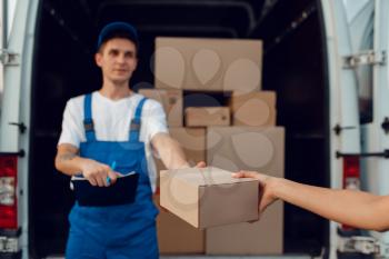 Deliveryman in uniform gives parcel to female buyer at the car, delivery service, delivering. Man holding cardboard package near the vehicle, male deliver and woman, courier or shipping job