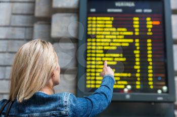 Female tourist looks on timetable on railway station, travel in Europe. Transportation by european railroads, passenger at the information display, comfortable tourism and travelling