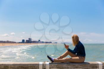Female tourist sitting on pier on city beach, sea coast, Europe. Summer tourism and travels, famous and popular places for vacation tour or holidays