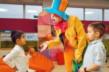 Funny clown animator dancing with little boys in kindergarten. Birthday celebrating in playroom, baby holiday in playground. Childhood happiness, childish leisure