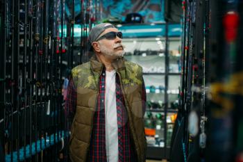 Fisherman in sunglasses choosing rod in fishing shop. Equipment and tools for fish catching and hunting, accessory choice on showcase in store