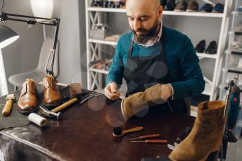 Shoemaker stitches the shoe, footwear repair service. Craftsman skill, shoemaking workshop, master works with boots