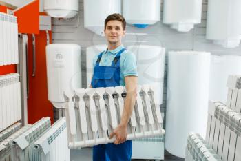 Plumber in uniform holds water heating radiator in plumbering store. Man buying sanitary engineering in shop