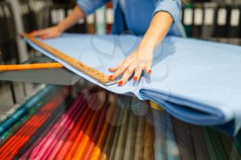 Woman measures the fabric in textile store. Shelf with cloth for sewing on background, clothing patterns choice in shop