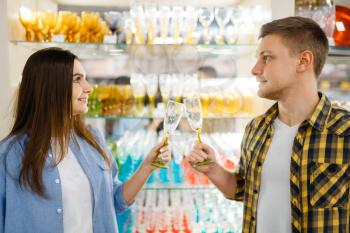 Young couple at the shelf with wineglasses in houseware store. Man and woman buying home goods in market, family in kitchenware supply shop