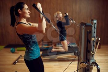 Two women on pilates training on exercise machine in gym, flexibility. Fitness workuot in sport club. Athletic female person, aerobics indoor, body stretching