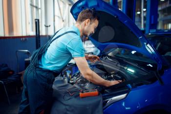 Auto electrician in uniform checks electrical circuits on car service station. Automobile checking and inspection, professional diagnostics and repair